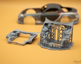 May include: A disassembled gray model car with detailed internal components. The image shows the car's body, chassis, and engine components, highlighting the intricate design of the model. The background is a solid orange color.