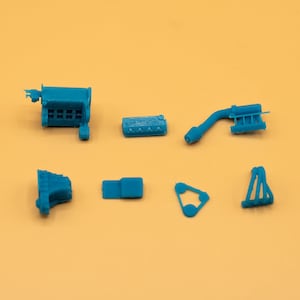 Op de afbeelding: Een set blauwe 3D-geprinte model auto-motoronderdelen. De set bevat een blok, een inlaatspruitstuk, een uitlaatspruitstuk, klepdeksels en andere onderdelen.