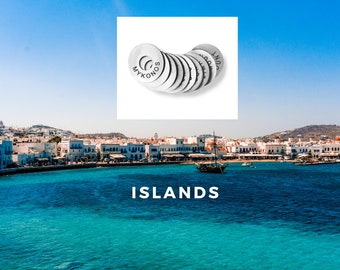 Könnte beinhalten: Eine Sammlung von silbernen Schlüsselanhängern aus Metall mit den Namen griechischer Inseln, darunter Mykonos, Santorini und Kreta, vor dem Hintergrund eines blauen Himmels und einer weiß getünchten Stadt auf einer griechischen Insel.