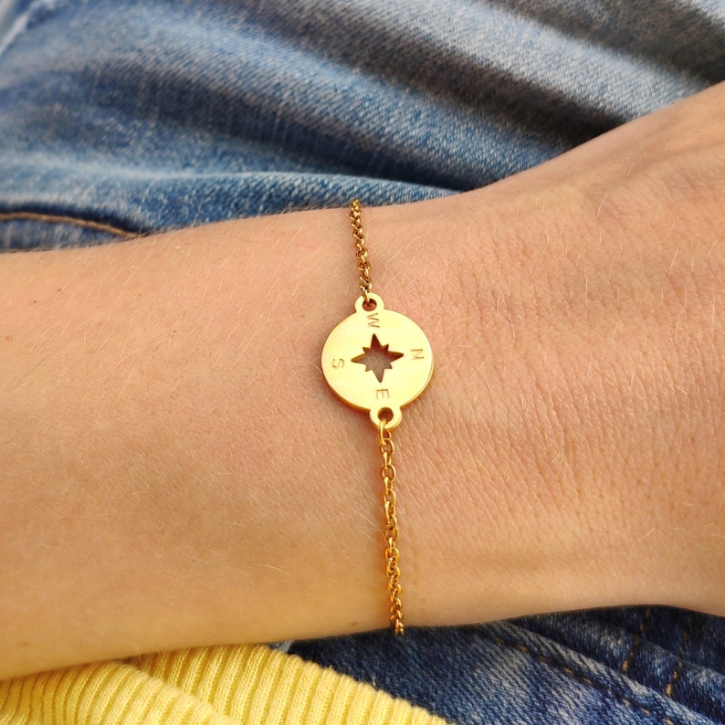 May include: Gold compass bracelet with a star in the center and the letters N, S, E, and W around the edge.