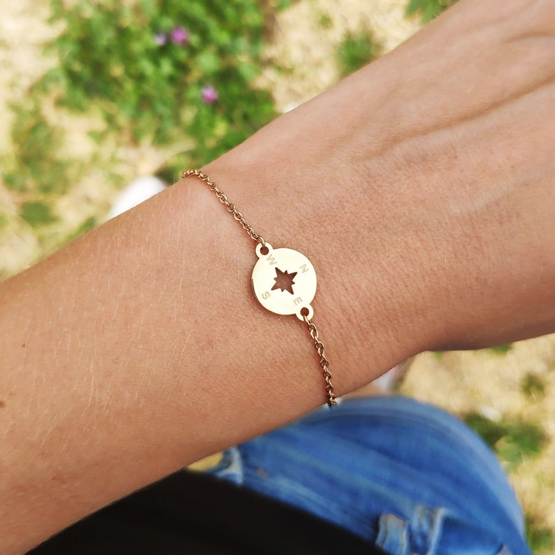 May include: A gold compass charm bracelet with a delicate chain. The compass charm has a star in the center and the letters N, S, E, and W around the edge.