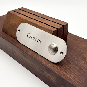 Könnte beinhalten: Ein silberner Türklingelknopf mit der Gravur "Gravur" auf einem Holzsockel.