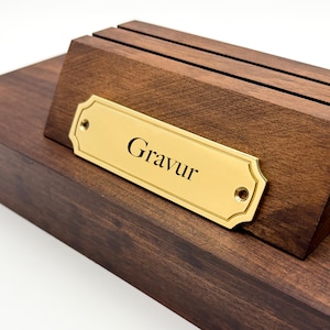 Könnte beinhalten: Eine Holzplakette mit einer Messingplatte, auf der "Gravur" steht.