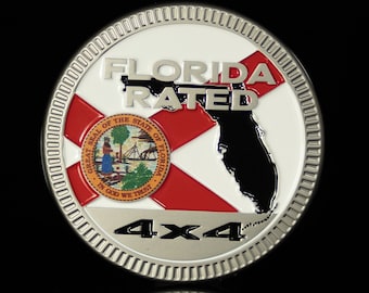 Può includere: Un emblema rotondo color argento con le parole "FLORIDA RATED" e un contorno nero della Florida. L'emblema presenta la bandiera e il sigillo dello stato della Florida, con "4x4" sotto. Lo sfondo è nero.