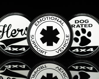 Può includere: Tre emblemi circolari bianchi e neri con bordi scanalati. L'emblema centrale presenta un simbolo della stella della vita e il testo EMOTIONAL SUPPORT VEHICLE. L'emblema a sinistra mostra il testo Hers e 4x4. Quello a destra mostra un'impronta e DOG RATED 4x4.