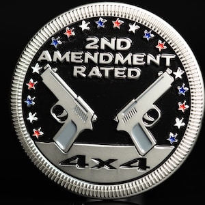May include: A silver-coloured round coin with a black background. The coin has a design of two crossed pistols with the text "2ND AMENDMENT RATED 4X4" and a ring of stars around the edge.