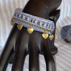 Puede incluir: Un brazalete de mezclilla azul con una cadena y dijes de corazón dorados.