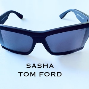 Może przedstawiać: Czarne okulary przeciwsłoneczne Sasha Tom Ford z ciemnymi soczewkami. Okulary mają grubą, kanciastą oprawkę i nowoczesny design. Tekst "SASHA TOM FORD" jest wyświetlany poniżej.