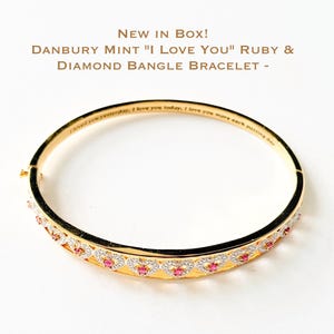 Könnte beinhalten: Ein goldfarbenes Armreif-Armband mit herzförmigen Rubinen und Diamanten. Auf dem Armband steht der Text "I loved you yesterday, I love you today, I love you more each passing day". Der Text "NEW IN BOX! DANBURY MINT "I LOVE YOU" RUBY & DIAMOND BANGLE BRACELET -" steht oben.