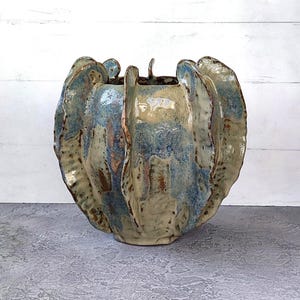 May include: A ceramic vase with a unique, organic shape. The vase features a blend of blue, beige, and brown hues, with a textured surface. The design includes petal-like edges, creating an artistic and sculptural appearance. A decorative piece for home decor.