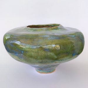 May include: A green and blue ceramic vase with a wide, rounded base and a narrow opening. The vase has a glossy finish and a unique, organic shape.