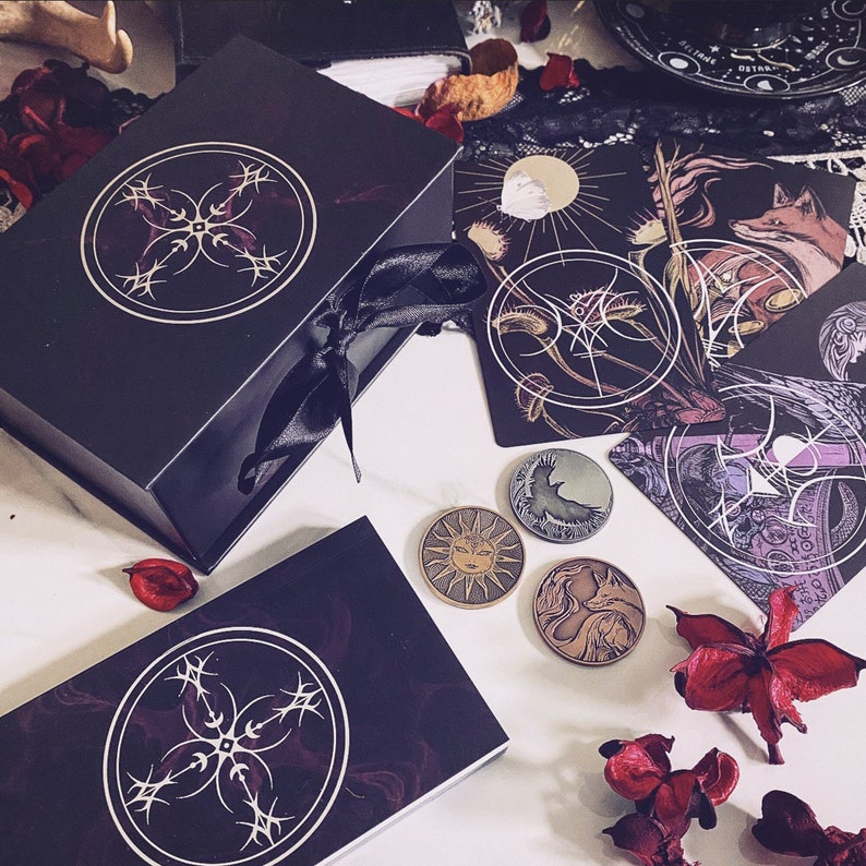 May include: A black box with a silver design on the lid, two smaller black boxes with silver designs, and five silver tokens with different designs. The tokens are on a white surface with red flowers.