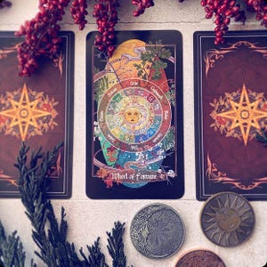 K&ouml;nnte beinhalten: Tarotkarte, die das Rad des Schicksals darstellt, ein kreisf&ouml;rmiges Design mit einer Sonne in der Mitte und Symbolen darum herum. Die Karte ist dunkelblau mit goldenen Akzenten und dem Text "Rad des Schicksals" unten.