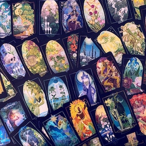 K&ouml;nnte beinhalten: Eine Sammlung von Tarotkarten mit bunten Illustrationen und goldenen Akzenten. Die Karten sind in einem zuf&auml;lligen Muster angeordnet, wobei sich einige Karten &uuml;berlappen. Die Karten sind alle oval geformt und haben einen schwarzen Hintergrund.