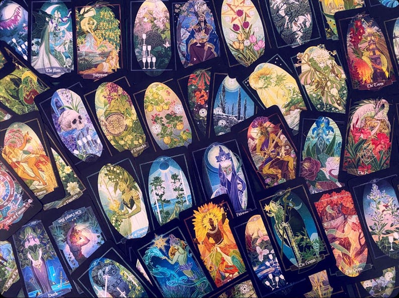 K&ouml;nnte beinhalten: Eine Sammlung von Tarotkarten mit bunten Illustrationen und goldenen Akzenten. Die Karten sind in einem zuf&auml;lligen Muster angeordnet, wobei sich einige Karten &uuml;berlappen. Die Karten sind alle oval geformt und haben einen schwarzen Hintergrund.
