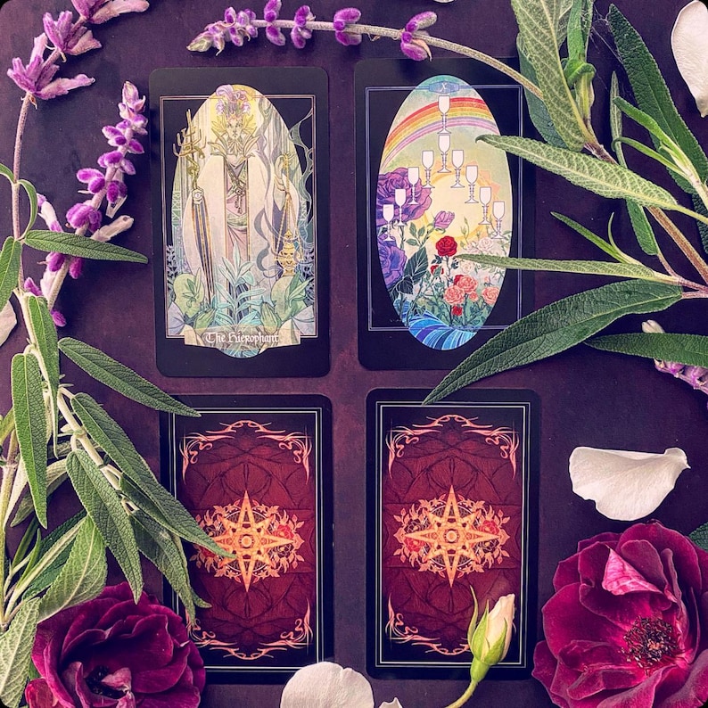 K&ouml;nnte beinhalten: Vier Tarotkarten auf einem violetten Hintergrund mit Blumen und Bl&uuml;tenbl&auml;ttern. Die Karten sind Der Kaiser, Zehn der Kelche, Der Stern und Die Welt. Die Karten sind schwarz mit goldenen Akzenten und zeigen farbenfrohe Illustrationen.