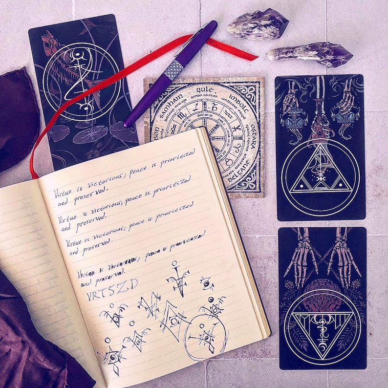 May include: An open notebook with handwritten text about virtue and peace. The notebook is surrounded by tarot cards with black and white illustrations of skeletons and geometric shapes. The text in the notebook reads: "Virtue is victorious; peace is prioritized and preserved."  "Virtue is victorious, peace is prioritized and preserved."  "Virtue is victorious; peace is prioritized and preserved."  "Victor is hotaraans; peace is prioritized and prasarval."  "VRTSZD"