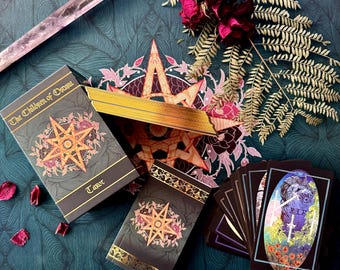 May include: A tarot deck box with gold accents and the text "The Children of Osiris Tarot" on the front. The box is open and the cards are visible. The cards are black with gold accents and feature intricate designs.