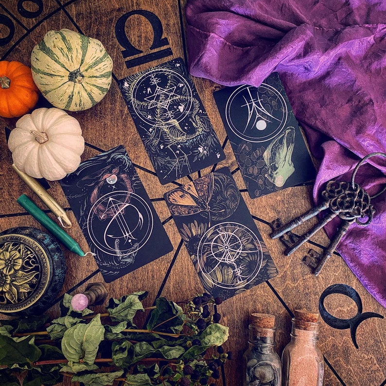 May include: A tarot card reading spread with a purple cloth, a wooden board with a symbol, and several cards with intricate designs. The cards feature a variety of symbols, including a star, a crescent moon, and a key.