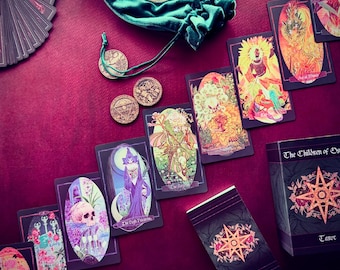 Puede incluir: Una baraja de tarot con una bolsa de terciopelo verde y monedas. Las cartas presentan ilustraciones de hadas, flores y otras imágenes místicas. La caja de la baraja tiene el texto "The Children of the Gods Tarot" en la parte delantera.