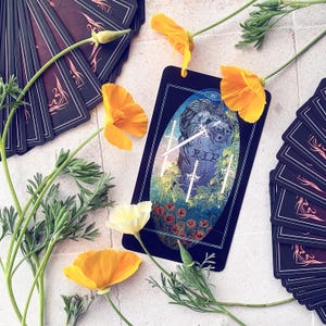 K&ouml;nnte beinhalten: Eine Tarotkarte mit schwarzem Hintergrund und einer blauen und gr&uuml;nen Illustration von drei Schwertern, die sich &uuml;ber einem Grabstein mit der Aufschrift "RIP" kreuzen. Die Karte ist von Blumen und anderen Tarotkarten umgeben.