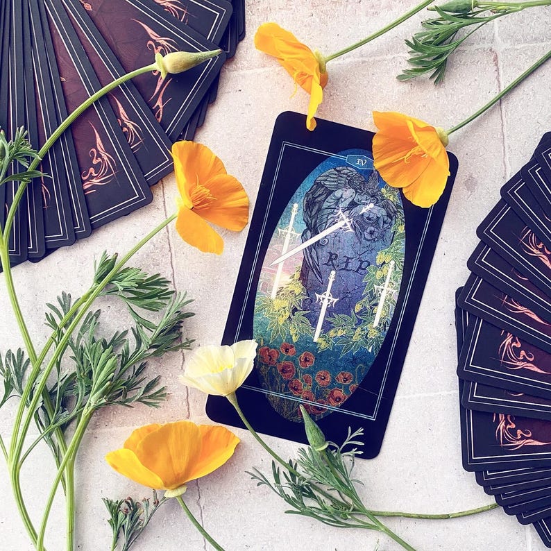 K&ouml;nnte beinhalten: Eine Tarotkarte mit schwarzem Hintergrund und einer blauen und gr&uuml;nen Illustration von drei Schwertern, die sich &uuml;ber einem Grabstein mit der Aufschrift "RIP" kreuzen. Die Karte ist von Blumen und anderen Tarotkarten umgeben.