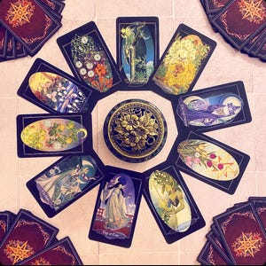 K&ouml;nnte beinhalten: Eine Tarotkarten-Lesespreizung mit 10 Karten, die in einem Kreis um einen dekorativen Metall-R&auml;ucherofen angeordnet sind. Die Karten sind schwarz mit goldenen Akzenten und zeigen Illustrationen von Blumen, Menschen und anderen Symbolen. Die Karten beinhalten "Die Kaiserin", "Die Hohepriesterin", "Der Page der Kelche" und "Der Stern".