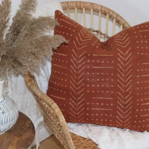 Puede incluir: Una almohada de color óxido con un patrón geométrico de líneas y puntos blancos sobre una silla de mimbre.