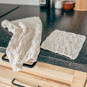 May include: Two white crocheted dishcloths, one folded and one laid flat, on a black countertop.
