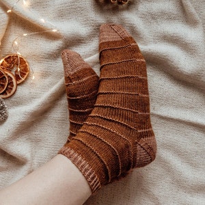 以下が含まれることがあります： 茶色とベージュのストライプ模様のニットソックスのペア。ソックスは柔らかく暖かい素材で作られており、冬の足元を暖かく保つのに最適です。