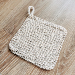May include: A white knitted pot holder with a loop handle. The pot holder is made of a soft, textured yarn.