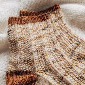 May include: A pair of knitted socks with a brown cuff and a speckled white and brown pattern.