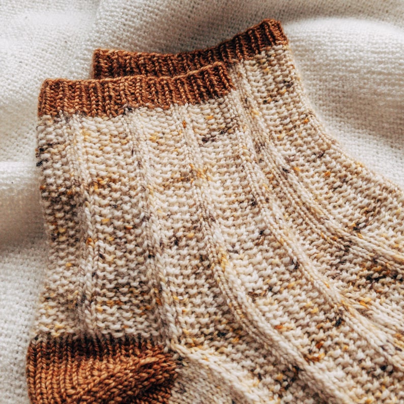 May include: A pair of knitted socks with a brown cuff and a speckled white and brown pattern.