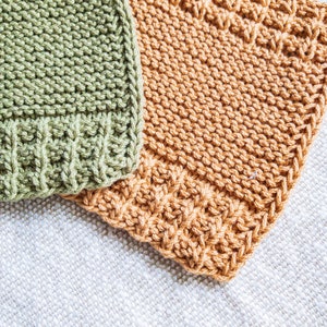 May include: Two knitted dishcloths, one green and one orange, are laid out on a white textured surface.