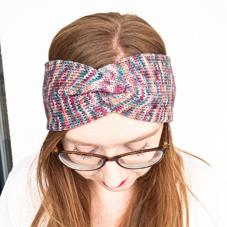 May include: A colorful knitted headband with a twisted knot design. The headband is made of a soft, warm yarn and features a variety of colors, including pink, blue, green, and purple.