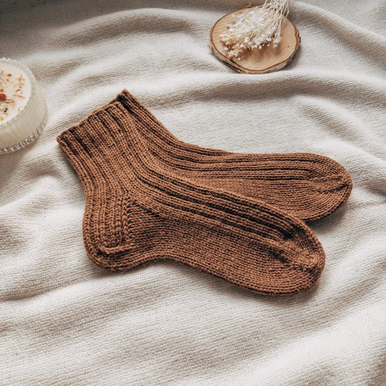 May include: A pair of brown knitted socks with a ribbed texture. The socks are folded and laid out on a white fabric background.