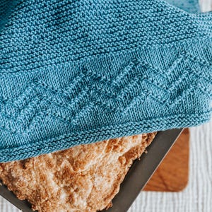 May include: A blue knitted dish towel covering a baking dish of golden brown bread.