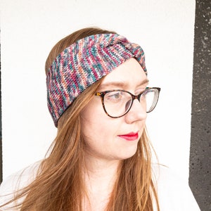 May include: A woman wearing a colorful knitted headband with a knot on top. She is wearing tortoiseshell glasses and has long brown hair.