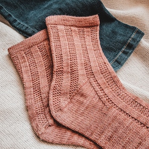 May include: A pair of knitted socks in a dusty rose color. The socks have a ribbed texture and are folded over at the top.