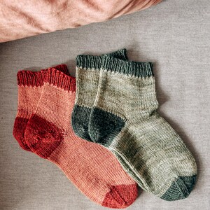 K&ouml;nnte beinhalten: Zwei Paar gestrickte Socken, ein Paar ist in hellrosa und rot, das andere Paar ist in gr&uuml;n und dunkelgr&uuml;n.