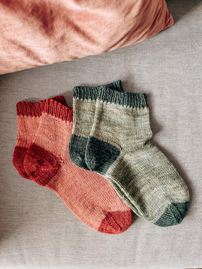 K&ouml;nnte beinhalten: Zwei Paar gestrickte Socken, ein Paar ist in hellrosa und rot, das andere Paar ist in gr&uuml;n und dunkelgr&uuml;n.