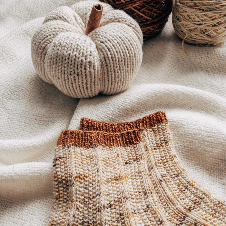 May include: A pair of knitted socks with a brown and white speckled pattern. The socks have a brown ribbed cuff.