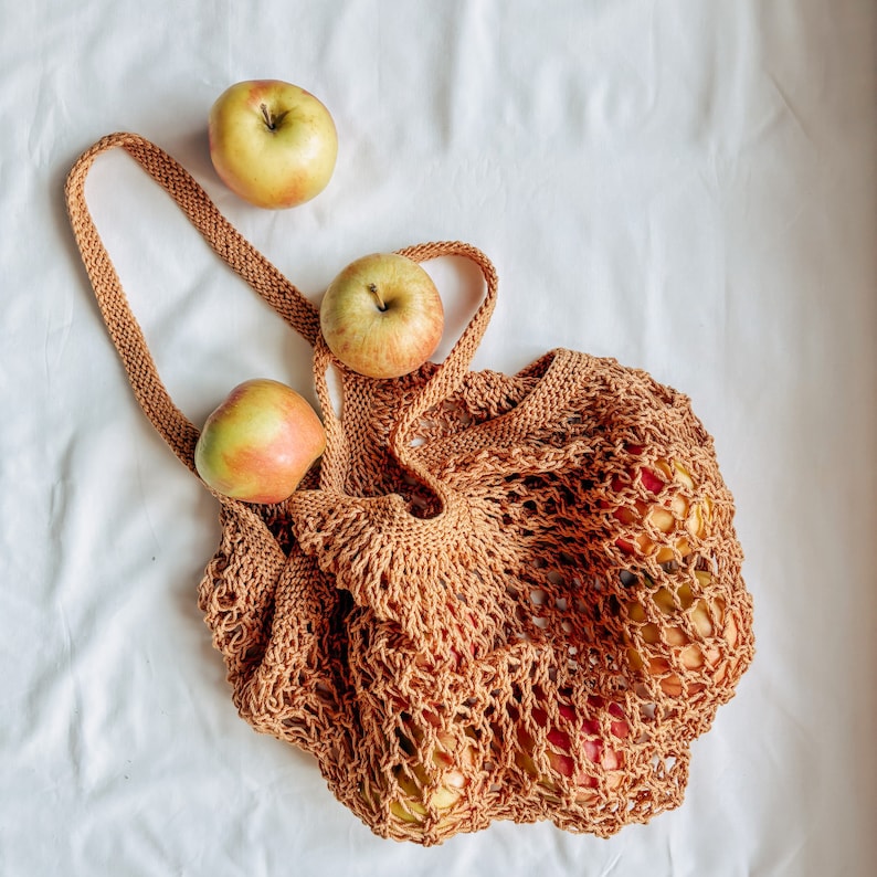 Peut inclure: Un sac de courses r&eacute;utilisable en tricot marron rempli de pommes. Le sac a une longue poign&eacute;e et est fait d'un mat&eacute;riau tiss&eacute;. Trois pommes sont plac&eacute;es pr&egrave;s du sac, avec un m&eacute;lange de peau rouge et verte.
