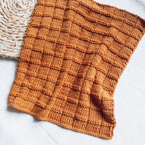 May include: A knitted throw blanket in a warm, burnt orange color. The blanket has a textured, waffle-like pattern.