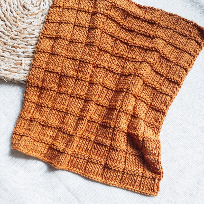 May include: A knitted throw blanket in a warm, burnt orange color. The blanket has a textured, waffle-like pattern.