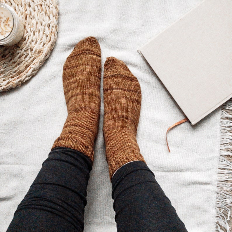 May include: A pair of brown knitted socks with a subtle marled pattern. The socks are worn by a person with black pants.