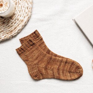 Puede incluir: Un par de calcetines de punto marrón con un sutil patrón jaspeado. Los calcetines están colocados sobre una superficie blanca.