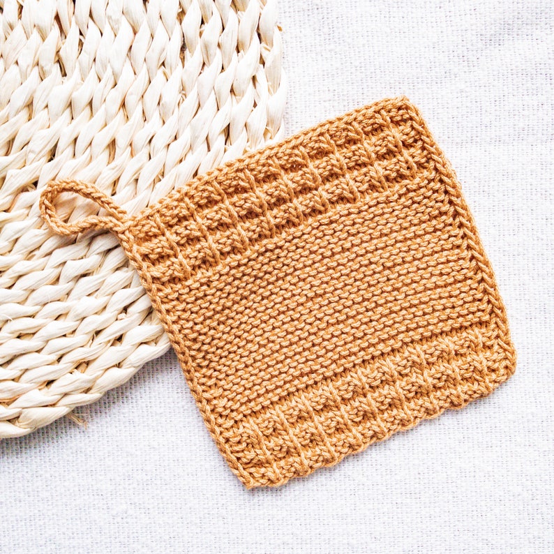 May include: A brown knitted dishcloth with a loop handle. The dishcloth is made with a textured stitch pattern.