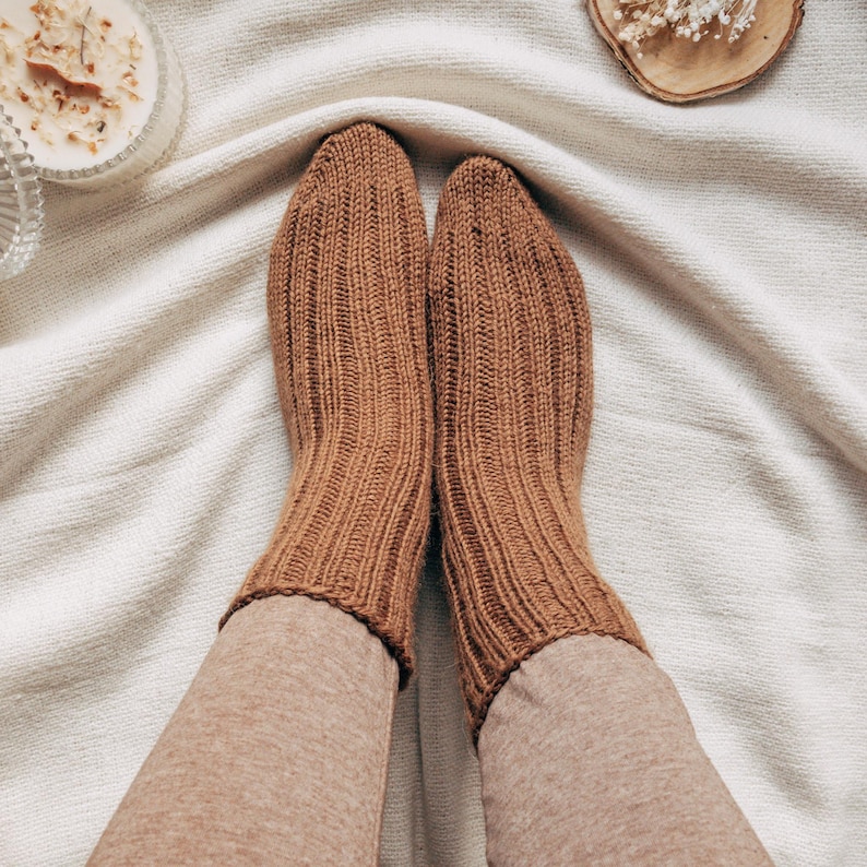 May include: A pair of brown ribbed knit socks. The socks are worn by a person sitting on a white blanket.