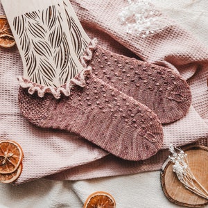 Puede incluir: Un par de calcetines de tobillo de punto rosa con ribete de encaje. Los calcetines están sobre una tela de tejido de waffle rosa.